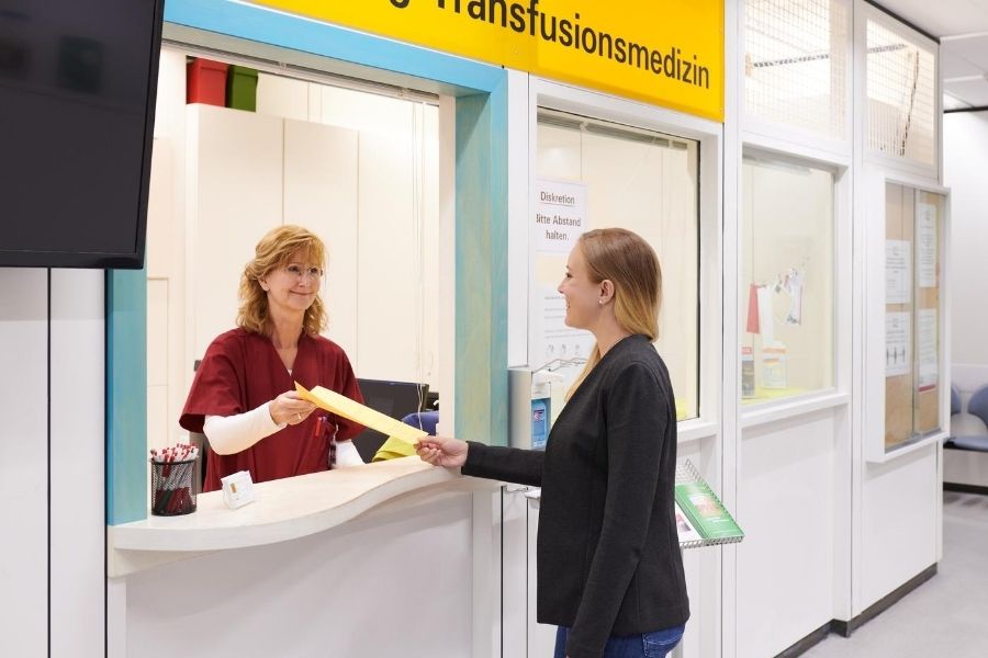 Sekretärin der Transfusionsmedizin überreicht Formular an Spenderin.